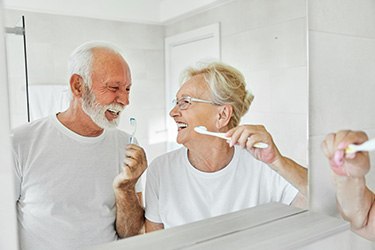 Senior couple smiling while brushing their teeth