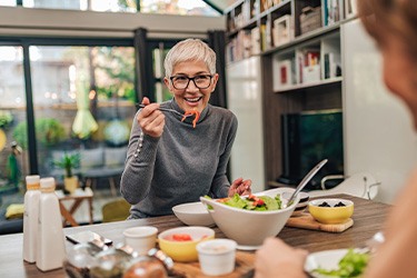 Woman smiling while eating lunch with friend in kitchen