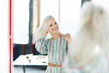 Woman smiling and getting ready for the day in front of a mirror