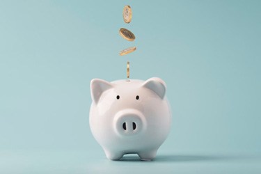 Coins dropping into a piggy bank on blue background