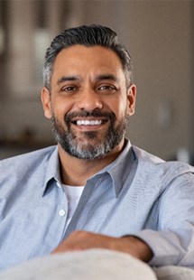 Mature man in blue button-up shirt smiling on couch