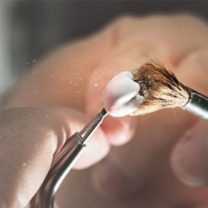 a lab technician brushing off a dental crown