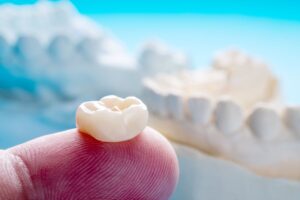 Closeup of a dental crown resting on a fingertip with a model of a jawbone blurry in the background